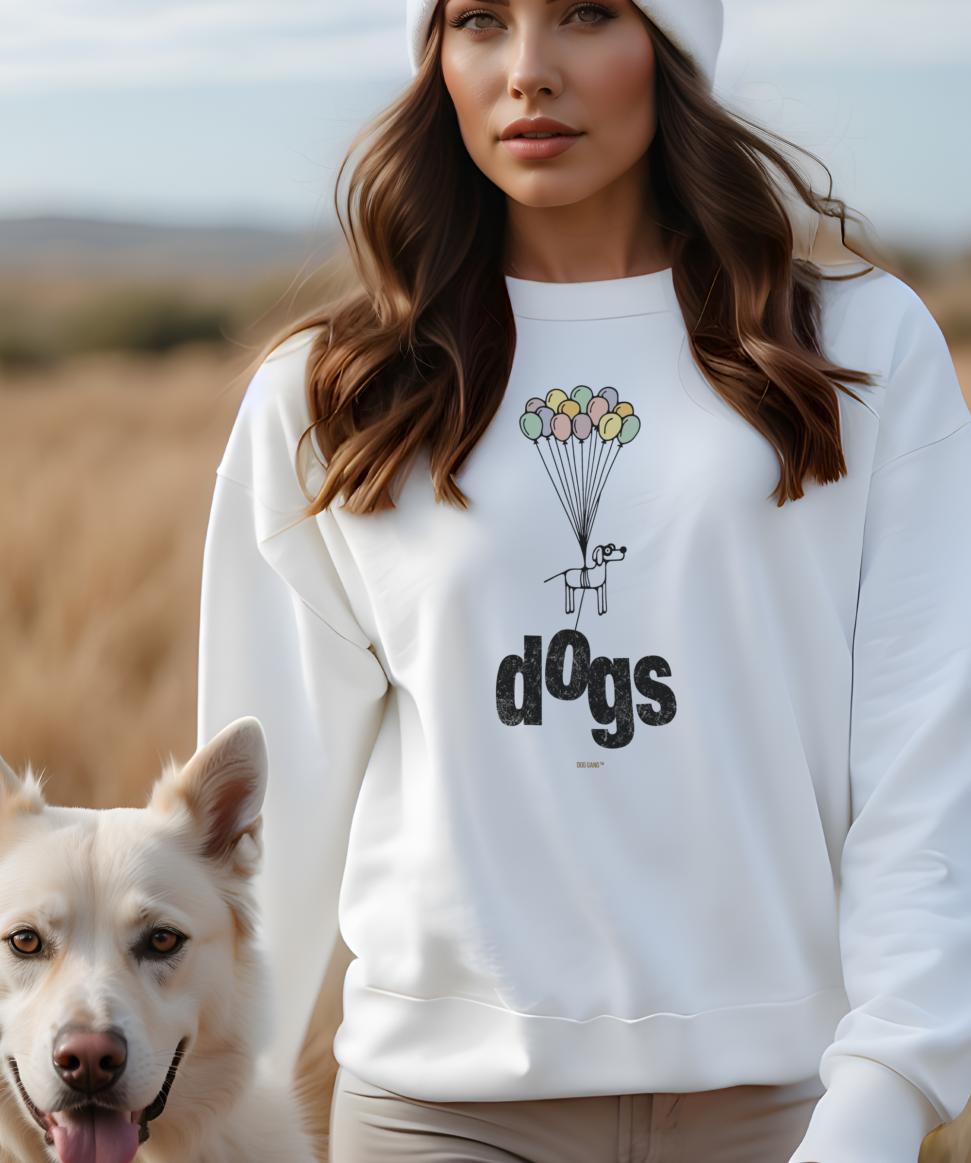 Eine Frau mit ihrem Hund in der Natur, die ein weißes Sweatshirt mit einem lustigen Motiv trägt, das einen Comic-Hund zeigt, der, von Luftballons getragen, leicht vom Boden abhebt und dabei den Buchstaben "o" vom darunterstehenden Wort "dogs" mitnimmt. Ein Sweatshirt aus der Serie "Minimalistic" designt von Dog Gang.
